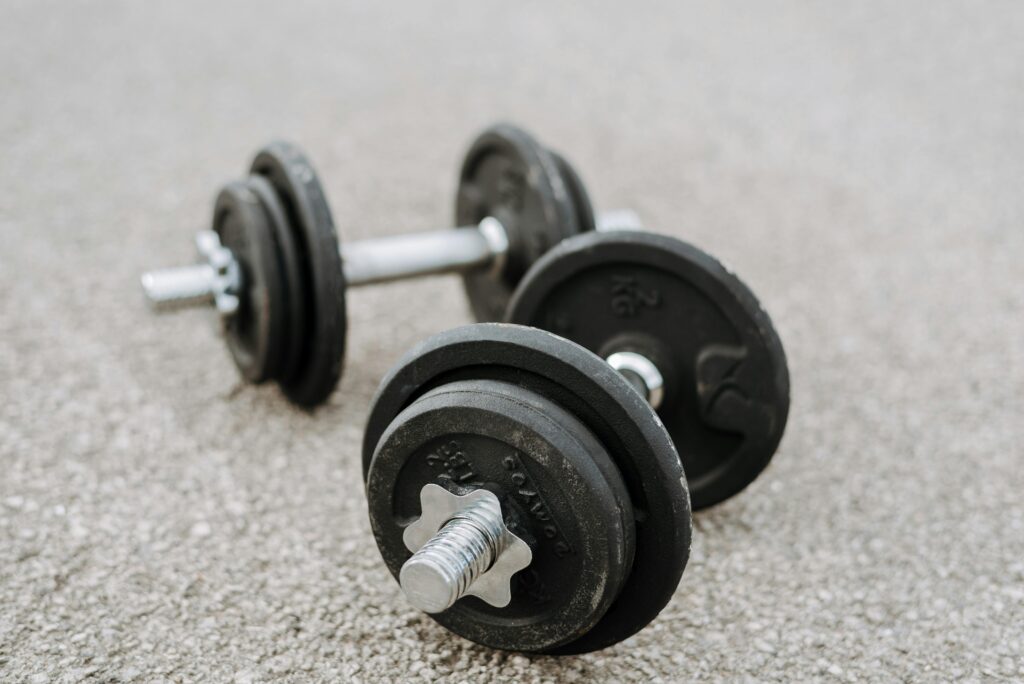 Black dumbbells on textured asphalt surface outdoors, showcasing fitness and strength concept.